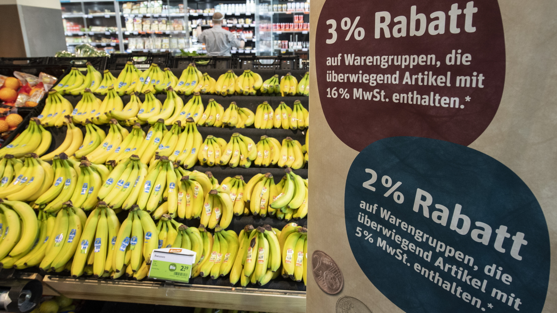 Ein Obstregal mit Bananen in einem Supermarkt und daneben ein Schild auf dem die Mehrwertsteuersenkungen erklärt wird.| Bildquelle: dpa